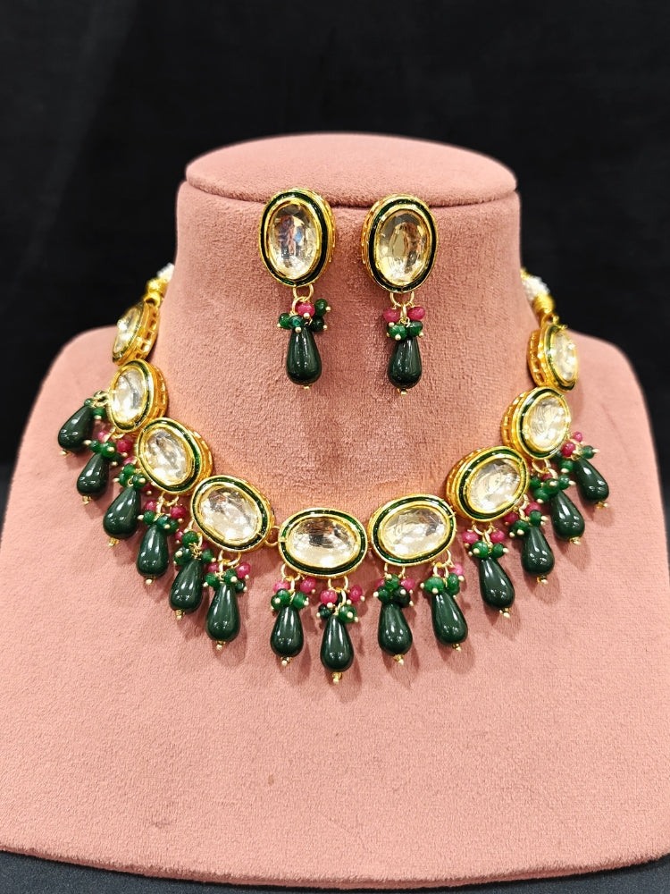 Close-up of an ornate traditional (Gold Polish) Dark Green Collar jewellery set and earrings with Kundan, Red and Green small beads and Tumble Stone. Mehendi ceremony look completed with a handcrafted Kundan jewelry set. Festive saree styling with a premium artificial Kundan necklace. Perfect Necklace for Wedding Function and Festive.