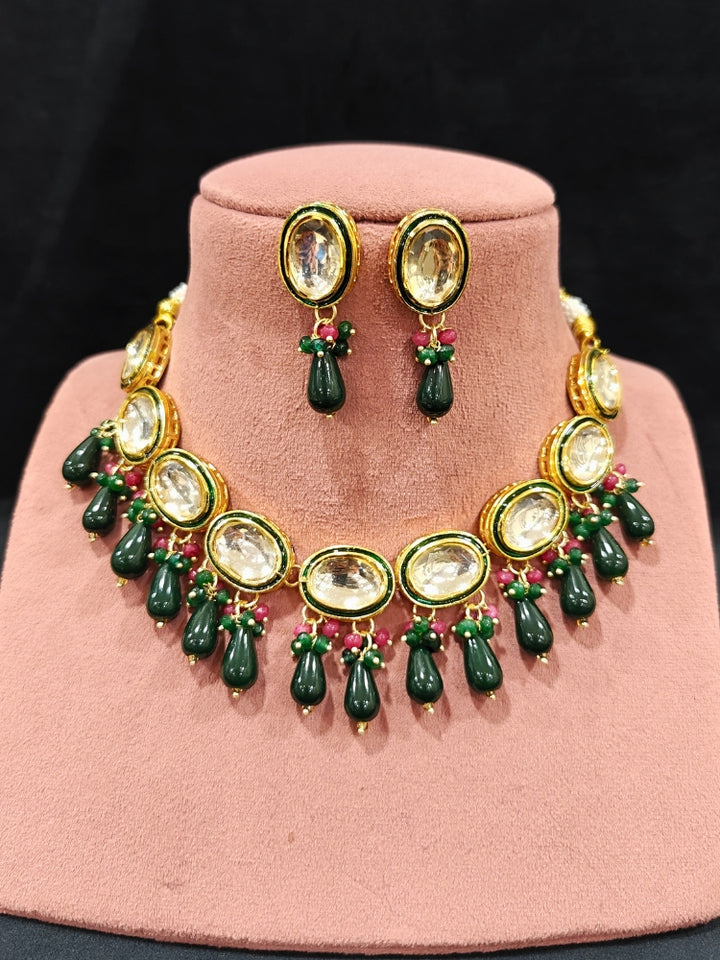 Close-up of an ornate traditional (Gold Polish) Dark Green Collar jewellery set and earrings with Kundan, Red and Green small beads and Tumble Stone. Mehendi ceremony look completed with a handcrafted Kundan jewelry set. Festive saree styling with a premium artificial Kundan necklace. Perfect Necklace for Wedding Function and Festive.