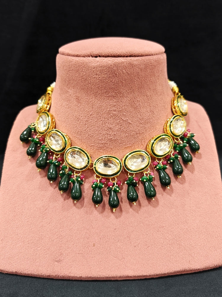 Close-up of an ornate traditional (Gold Polish) Dark Green Collar jewellery set and earrings with Kundan, Red and Green small beads and Tumble Stone. Mehendi ceremony look completed with a handcrafted Kundan jewelry set. Festive saree styling with a premium artificial Kundan necklace. Perfect Necklace for Wedding Function and Festive.