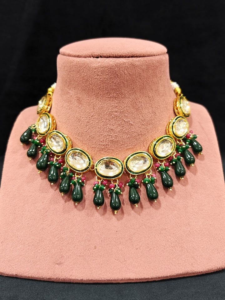 Close-up of an ornate traditional (Gold Polish) Dark Green Collar jewellery set and earrings with Kundan, Red and Green small beads and Tumble Stone. Mehendi ceremony look completed with a handcrafted Kundan jewelry set. Festive saree styling with a premium artificial Kundan necklace. Perfect Necklace for Wedding Function and Festive.