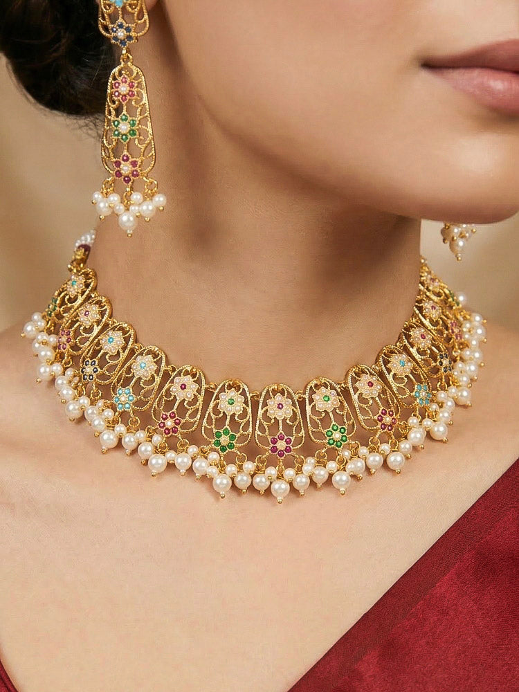 Close-up of a woman wearing an ornate traditional Navratan jadau gold jewellery set and jadau earrings with navratan color stone and Pearls. Woman pairing a traditional Jadau necklace with a silk saree. Woman wearing a royal Jadau necklace for festive events in India.