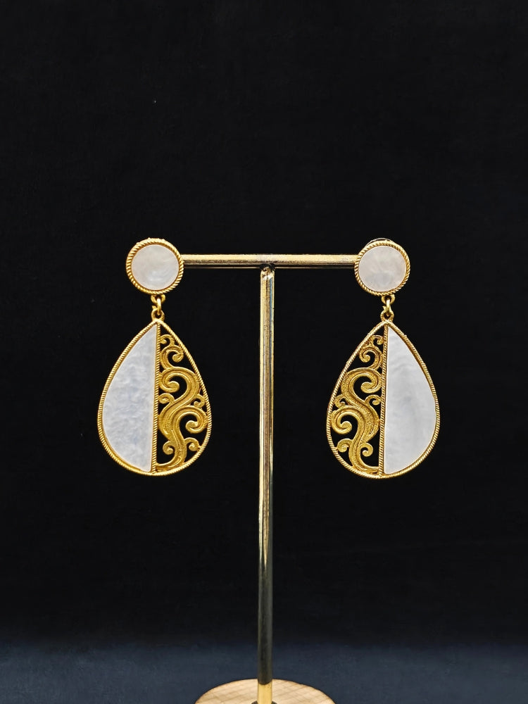 A close-up of the Chandsona Earrings—large teardrop earrings in Mother of Pearl and gold, with a round stud and ornate swirling detail. These modern, elegant White & Gold Earrings create a striking look.