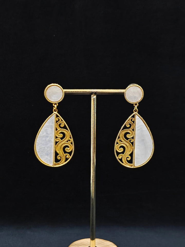 A close-up of the Chandsona Earrings—large teardrop earrings in Mother of Pearl and gold, with a round stud and ornate swirling detail. These modern, elegant White & Gold Earrings create a striking look.
