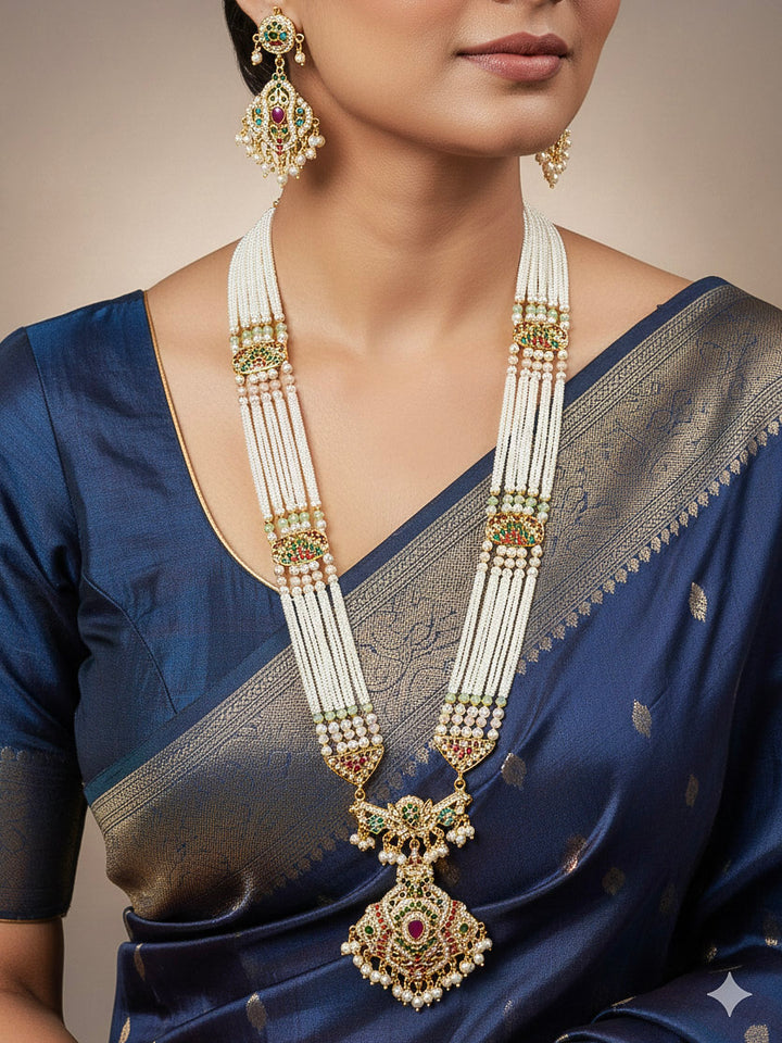 Close-up of a woman wearing an ornate traditional long jadau gold jewellery set and jadau earrings with pearls and gemstones. Perfect Jadau necklace set for weddings and festivals. 
