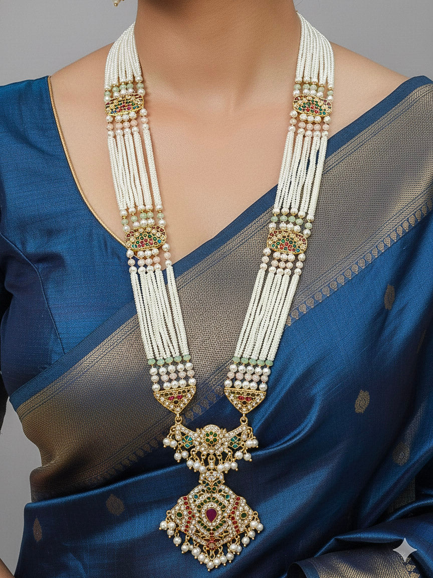 Close-up of a woman wearing a gold Indian traditional long jadau jewellery with pearls and multicolor jadau stones, and matching jadau earrings. This authentic jadau jewelry set can we worn as jadau necklace set for weddings. 