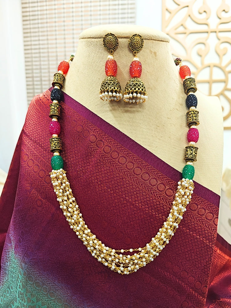 A mannequin showcases the Charvi Necklace Set—an elegant gold piece with oxidized brass beads, multicolored stones, with multiple strands of pearls, paired with matching jhumka earrings and styled with a maroon and purple saree—perfect for adding flair to any wedding ceremony.
