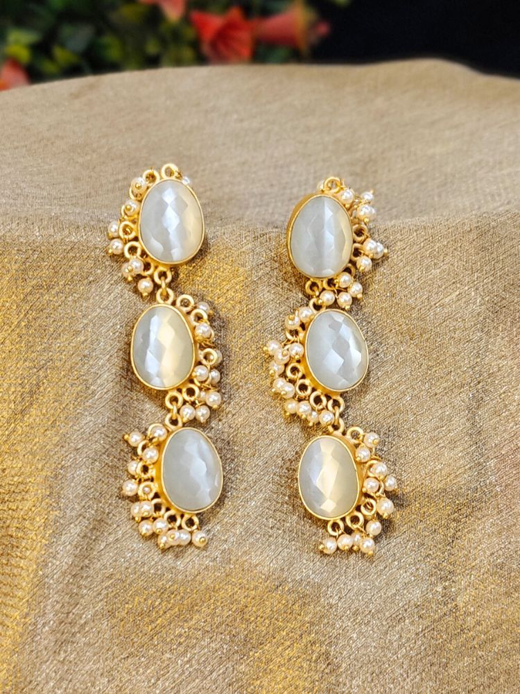 The Chloe long Earrings feature three oval milky stones on each piece, accented by  pearls and set against a golden fabric background—an elegant choice to complement your wedding ceremony dress.