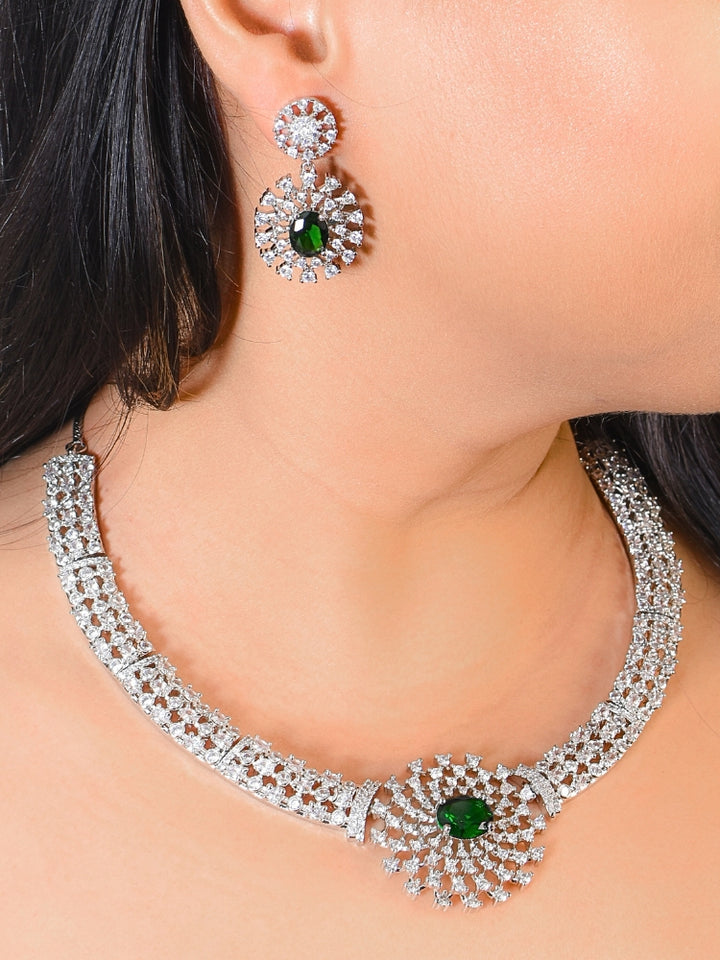 A woman adorns herself with the Cressida Green Necklace Set, featuring sparkling American Diamond necklace,  highlighted by a striking green gemstone in the center. This necklace set comes along with matching earrings. The jewelry intricate design elegantly enhances her look.