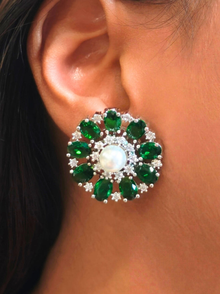 A close-up of a womans ear wearing the Dark Green Blossom stud Earrings—large, circular Dark Green earrings with a pearl at the center, colorful accents, and a border of sparkling American Diamonds. The stud earrings give a flower earrings feel. 