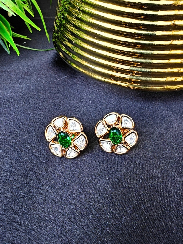 The Dark Green Daffodil stud Earrings feature gold flower-shaped brass settings with clear American Diamond petals and a Dark green stone center, displayed on a Black surface with Golden Aceent in the background.