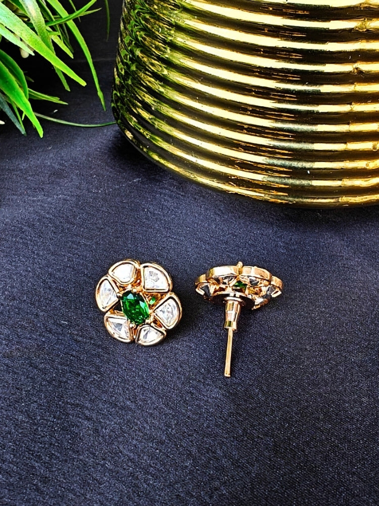 The Dark Green Daffodil stud Earrings feature gold flower-shaped brass settings with clear American Diamond petals and a Dark green stone center, displayed on a Black surface with Golden Aceent in the background.