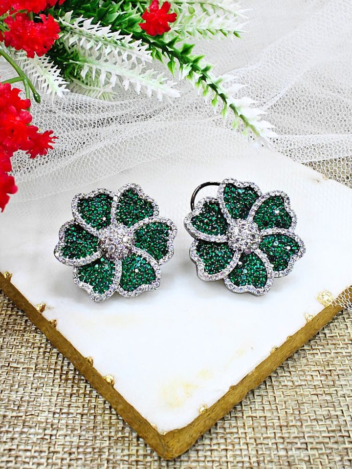 Dark Green Daisy Earrings, adorned with green colored stones and sparkling American Diamonds in close setting. They come with a classic flap at the back. The close setting earrings are showcased on a white marble slab with red and white artificial flowers—ideal for complementing your favorite cocktail gown. 