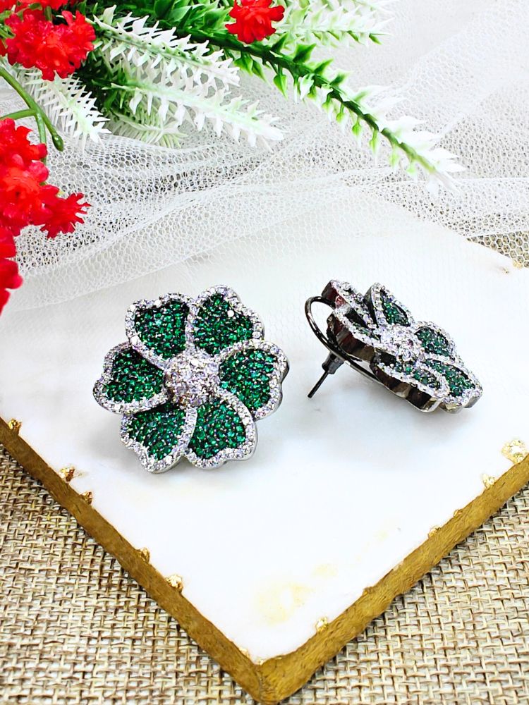 Dark Green Daisy Earrings, adorned with green colored stones and sparkling American Diamonds in close setting. They come with a classic flap at the back. The close setting earrings are showcased on a white marble slab with red and white artificial flowers—ideal for complementing your favorite cocktail gown. 