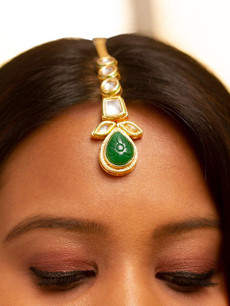 Close-up of a woman wearing an ornate traditional (Gold Polish) Dark Green Long Kundan jewellery set and earrings and a Choker and Mangtikka with Kundan and Colored Stones. Wedding celebration look enhanced with a statement Kundan necklace. Bride wearing a royal Kundan artificial necklace for wedding rituals.