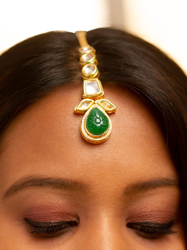 Close-up of a woman wearing an ornate traditional (Gold Polish) Dark Green Long Kundan jewellery set and earrings and a Choker and Mangtikka with Kundan and Colored Stones. Wedding celebration look enhanced with a statement Kundan necklace. Bride wearing a royal Kundan artificial necklace for wedding rituals.