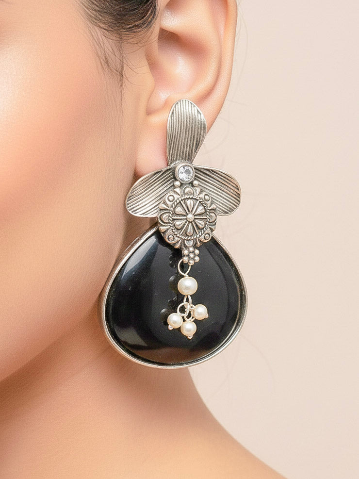Close-up of a woman wearing an ornate Western (Silver Polish) Black Oxidised Earrings with Black Colored Stone and Pearl. Festive Diwali look styled with premium artificial  Oxidised earrings. 
