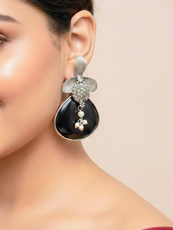 Close-up of a woman wearing an ornate Western (Silver Polish) Black Oxidised Earrings with Black Colored Stone and Pearl. Festive Diwali look styled with premium artificial  Oxidised earrings. 