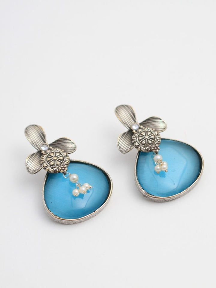 David Blue oxidized Earrings feature silver flower-shaped tops, decorative floral details, and blue teardrop stones. Small white pearls dangle at the center, adding a touch of elegance to these stylish german silver earrings.  Oxidized earrings from the oxidized jewelry collection. 