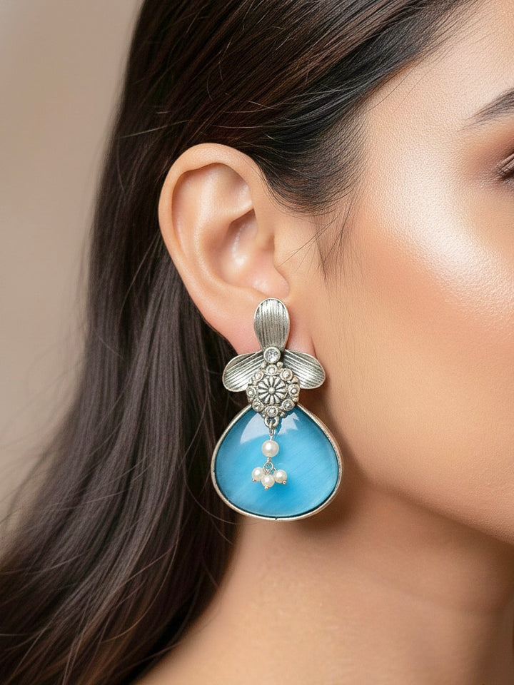 Close-up of a woman wearing an ornate Western (Silver Polish) Blue Oxidised Earrings with Blue Colored Stone and Pearl. Festive Diwali look styled with premium artificial  Oxidised earrings. 