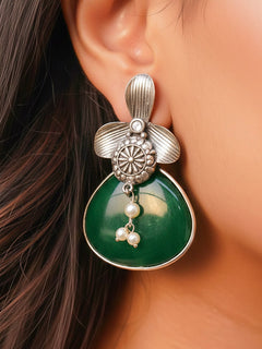 Close-up of a woman wearing an ornate Western (Silver Polish) Dark Green Oxidised Earrings with Dark Green Colored Stone and Pearl. Festive Diwali look styled with premium artificial  Oxidised earrings. 