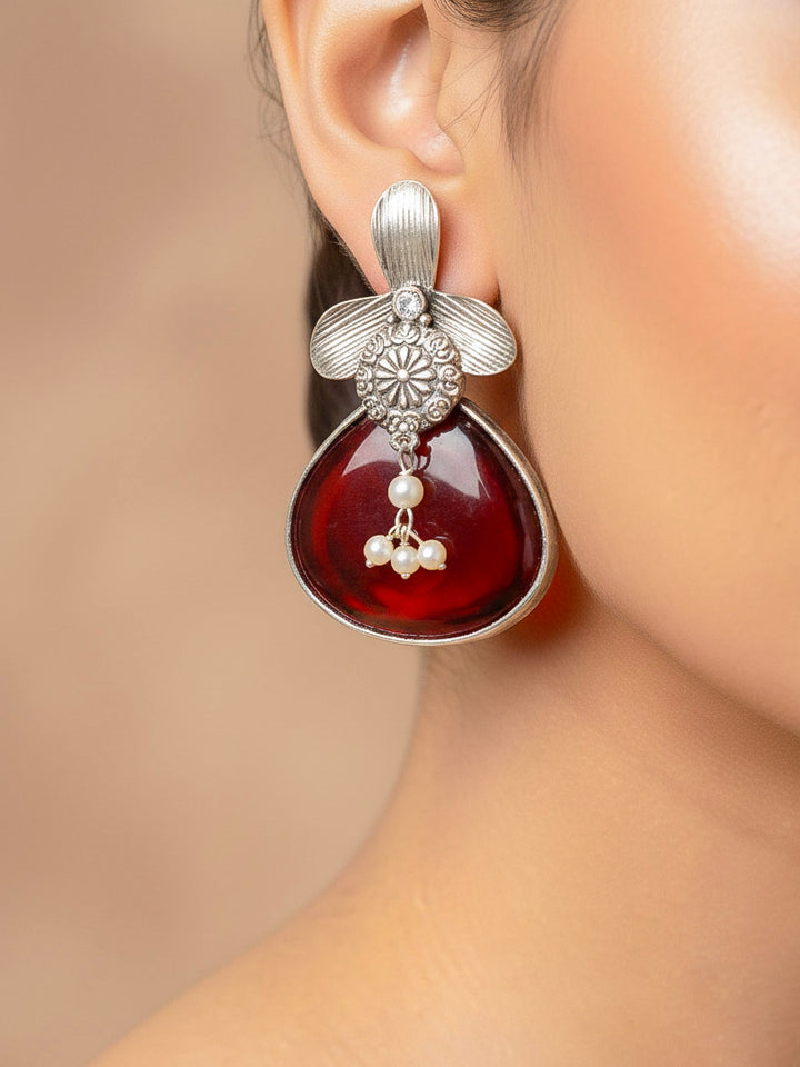 Close-up of a woman wearing an ornate Western (Silver Polish) Maroon Oxidised Earrings with Maroon Colored Stone and Pearl. Festive Diwali look styled with premium artificial  Oxidised earrings. 