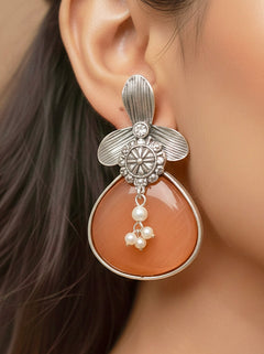 Close-up of a woman wearing an ornate Western (Silver Polish) Orange Oxidised Earrings with Orange Colored Stone and Pearl. Festive Diwali look styled with premium artificial  Oxidised earrings. 