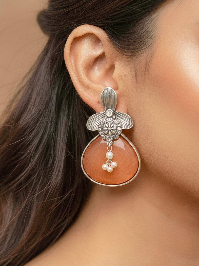 Close-up of a woman wearing an ornate Western (Silver Polish) Orange Oxidised Earrings with Orange Colored Stone and Pearl. Festive Diwali look styled with premium artificial  Oxidised earrings. 