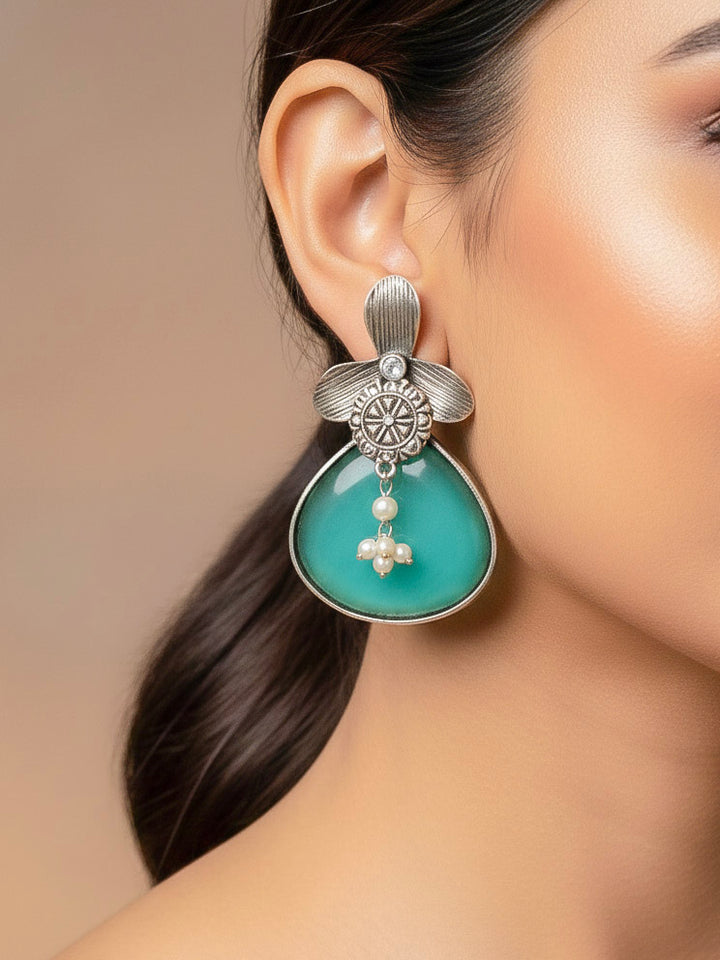 Close-up of a woman wearing an ornate Western (Silver Polish) Sea Green Oxidised Earrings with Sea Green Colored Stone and Pearl. Festive Diwali look styled with premium artificial Oxidised earrings. 