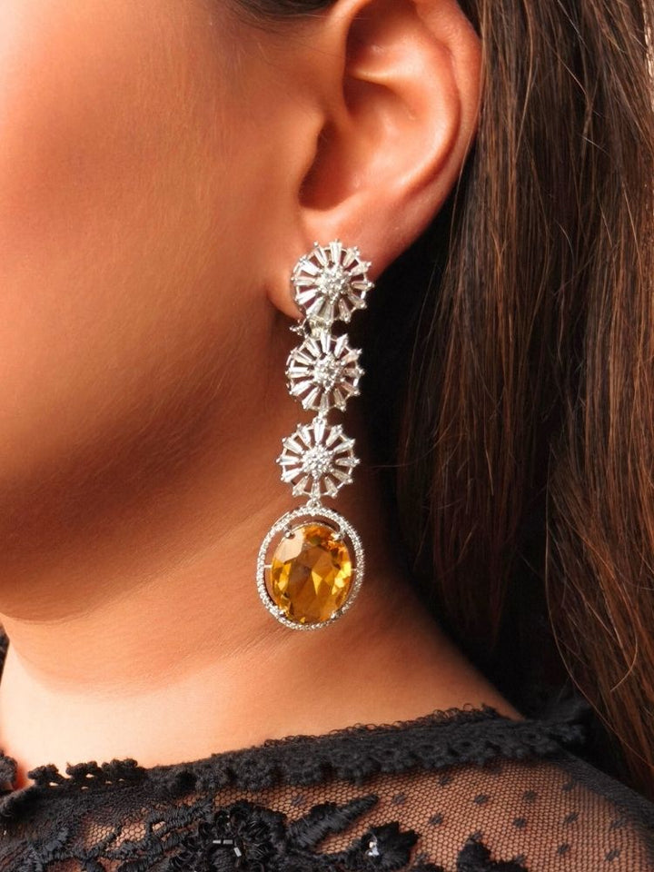 Close-up of a woman wearing the Delilah Earrings—yellow earrings featuring three sparkling, flower-shaped American Diamonds and a large oval shaped yellow gemstone at the bottom. She pairs them with a black lacy top, perfect for complementing a cocktail gown.