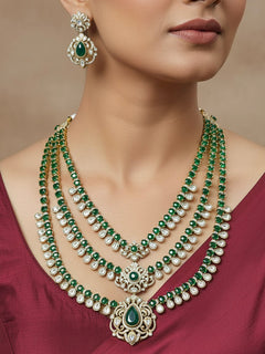 Close-up of a woman wearing an ornate traditional Green Heritage gold Long Layered jewellery set and earrings with colored Stone, Kundan and American Diamond. Mehendi ceremony styling featuring a premium heritage artificial jewelry piece. Woman styling a vintage heritage artificial necklace for a reception party.
