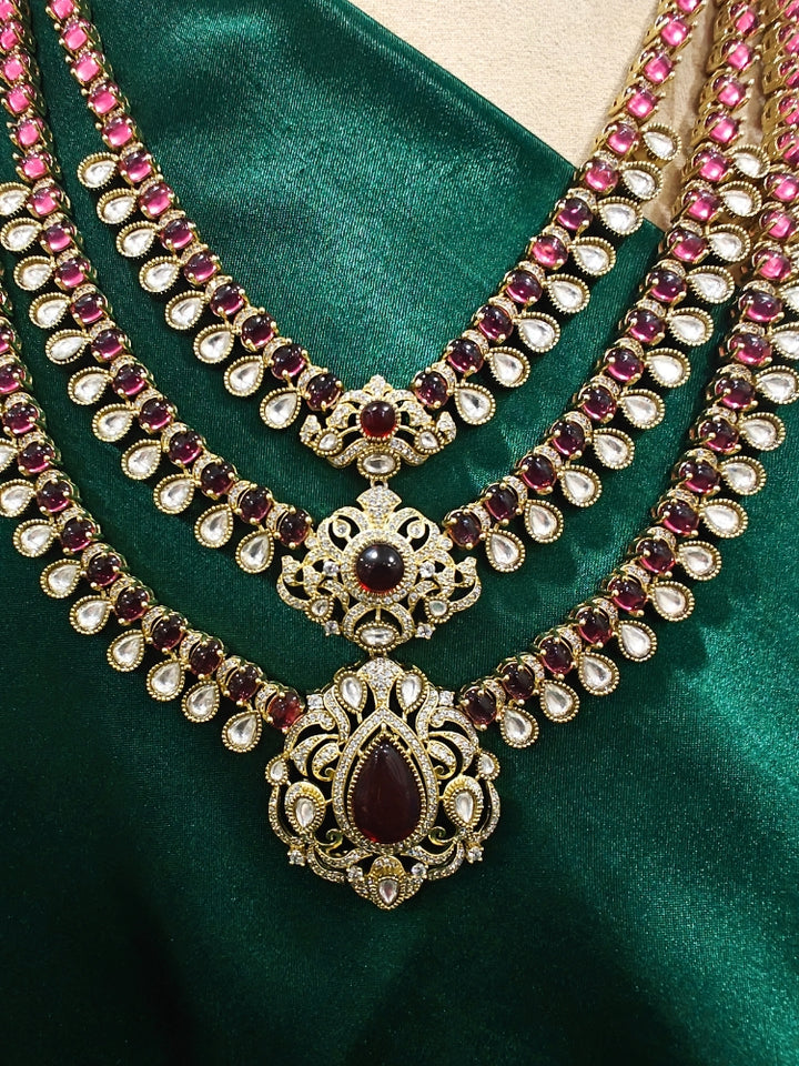 Close-up of an ornate traditional Red Heritage gold Long Layered jewellery set and earrings with colored Stone, Kundan and American Diamond. Mehendi ceremony styling featuring a premium heritage artificial jewelry piece. Traditional Indian look completed with a heritage artificial jewelry set.