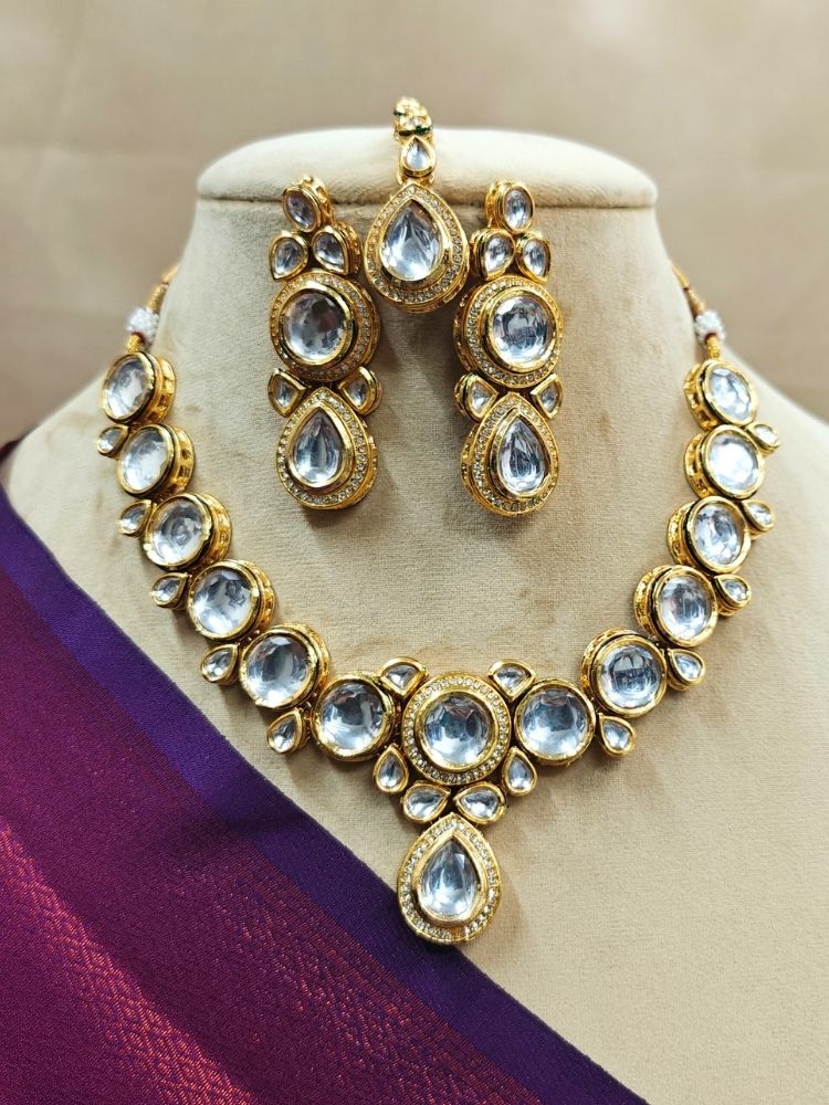 White Dhara Kundan Necklace Set—gold jewelry with White, and clear Monalisa stones—complete with necklace, earrings, and maang tikka adorned with american diamonds encircling some of the kundan stones. Shown on a cream dummy with purple saree. 