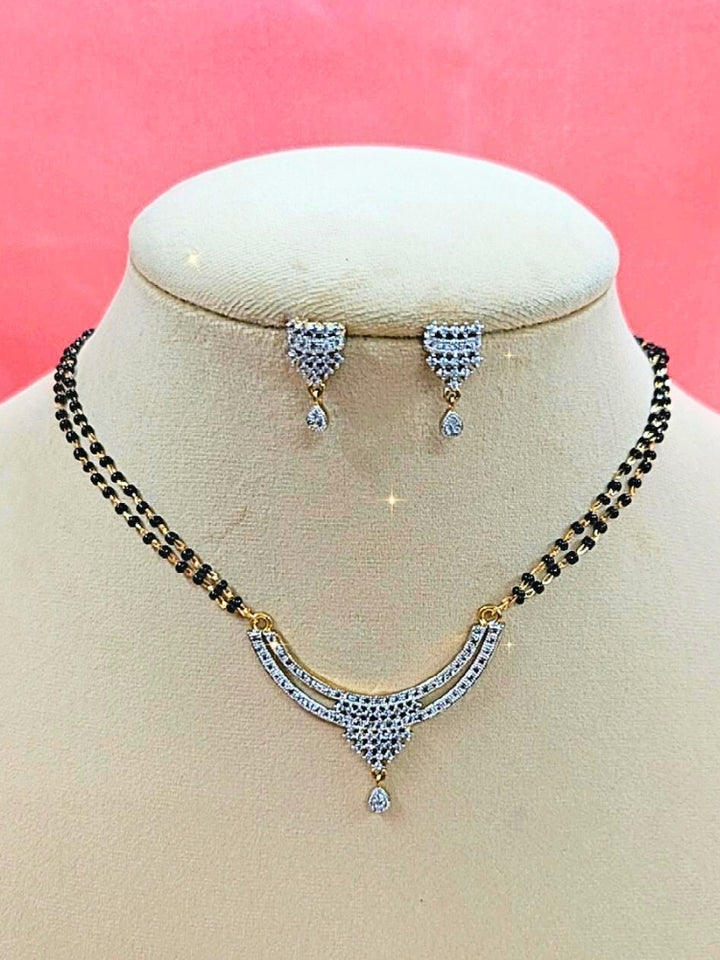 Diksha Mangalsutra—a gold necklace with black mangalsutra beads and matching earrings, pendant featuring sparkling American Diamonds—set against a cream dummy, perfect for your wedding ceremony dress. Diamond mangalsutra. Modern mangalsutra. 