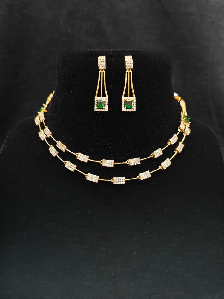 Close-up of an ornate Indo-western Green (gold Polish) Collar Layered Diamond jewellery set and earrings with American Diamond and Colored Stone. Party wear outfit completed with a lightweight American diamond necklace. Reception-ready look featuring a statement American diamond jewelry set.