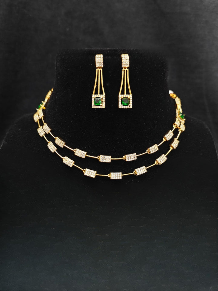 Close-up of an ornate Indo-western Green (gold Polish) Collar Layered Diamond jewellery set and earrings with American Diamond and Colored Stone. Party wear outfit completed with a lightweight American diamond necklace. Reception-ready look featuring a statement American diamond jewelry set.
