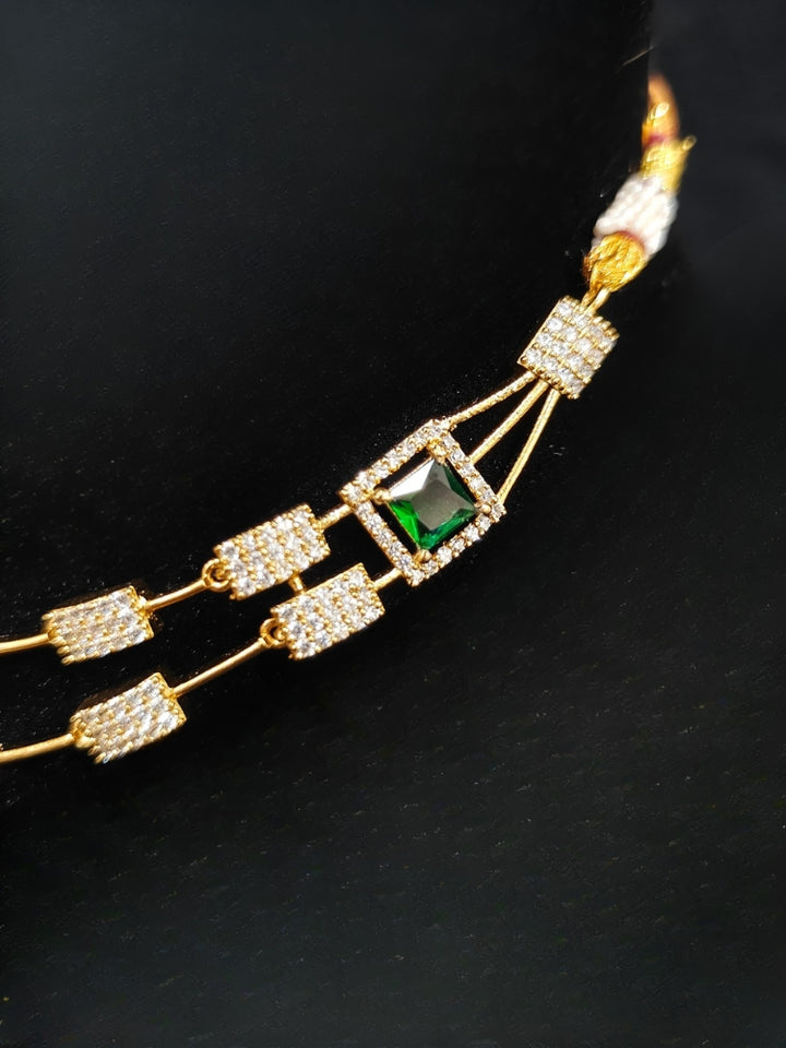 Close-up of an ornate Indo-western Green (gold Polish) Collar Layered Diamond jewellery set and earrings with American Diamond and Colored Stone. Party wear outfit completed with a lightweight American diamond necklace. Reception-ready look featuring a statement American diamond jewelry set.