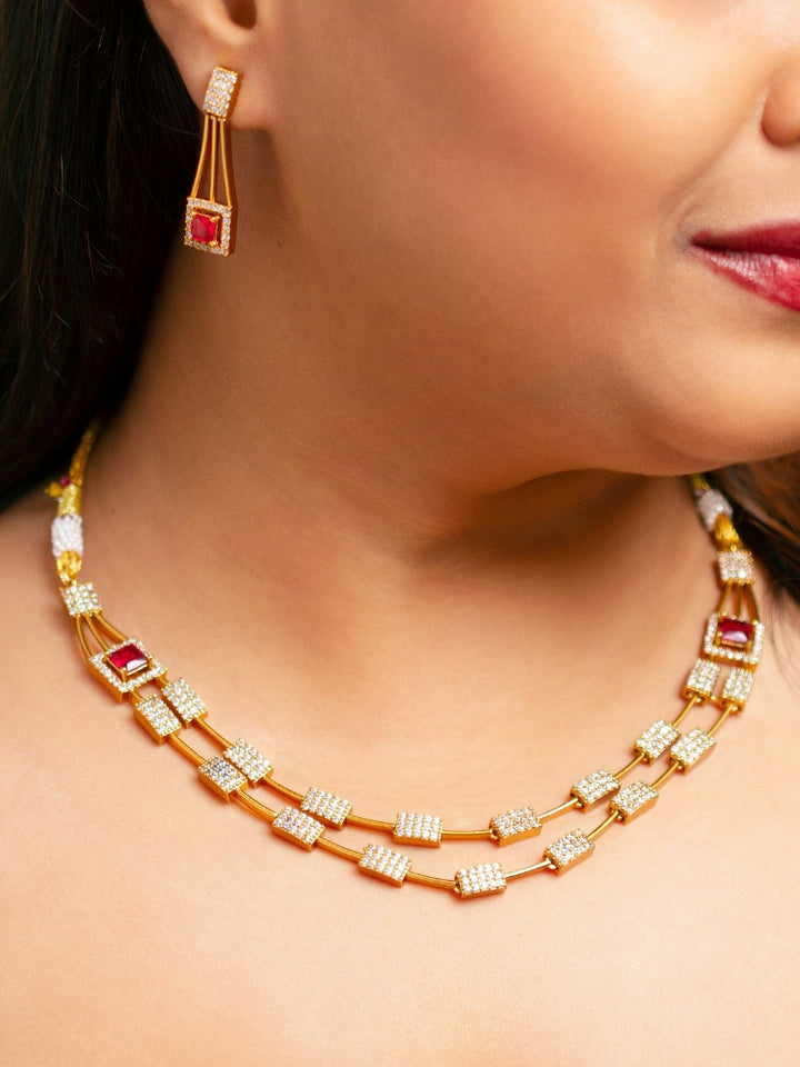 A woman wears the Diora Red Necklace Set, a gold party jewelry set featuring a red 2 layer necklace set made with  American diamonds and red gemstones at both the corners, paired with matching earrings. Only her lower face and neck are visible.