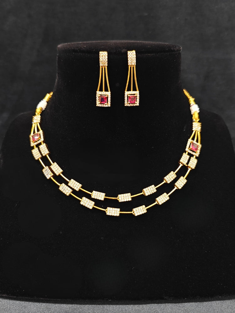 Close-up of an ornate Indo-western Red (gold Polish) Collar Layered Diamond jewellery set and earrings with American Diamond and Colored Stone. Party wear outfit completed with a lightweight American diamond necklace. Reception-ready look featuring a statement American diamond jewelry set.