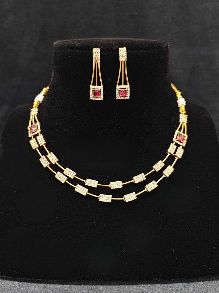 Close-up of an ornate Indo-western Red (gold Polish) Collar Layered Diamond jewellery set and earrings with American Diamond and Colored Stone. Party wear outfit completed with a lightweight American diamond necklace. Reception-ready look featuring a statement American diamond jewelry set.