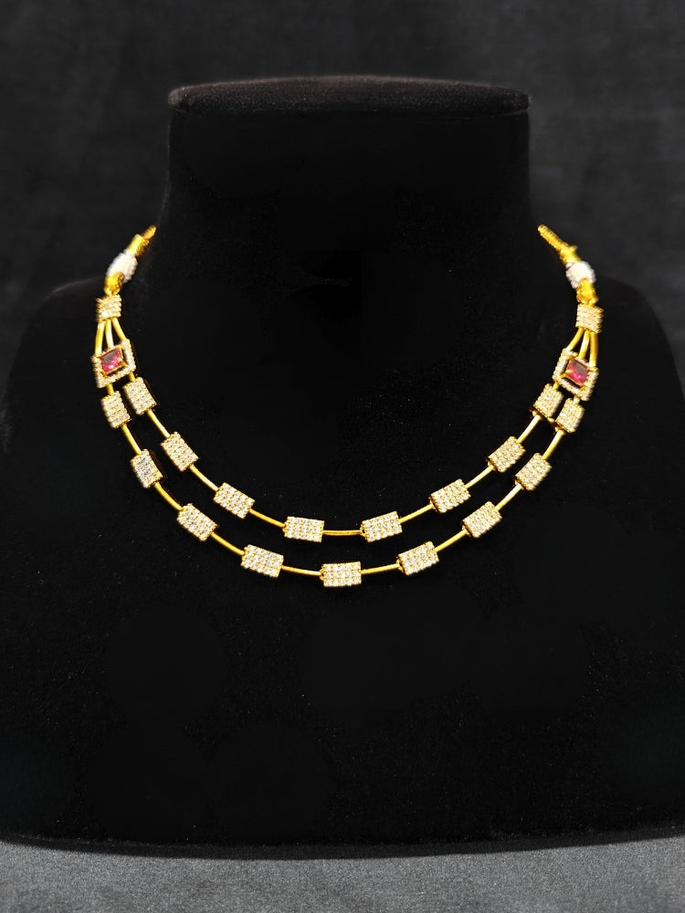 Close-up of an ornate Indo-western Red (gold Polish) Collar Layered Diamond jewellery set and earrings with American Diamond and Colored Stone. Party wear outfit completed with a lightweight American diamond necklace. Reception-ready look featuring a statement American diamond jewelry set.