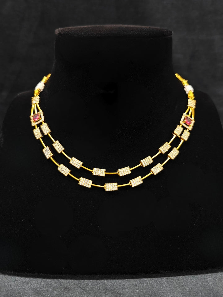 Close-up of an ornate Indo-western Red (gold Polish) Collar Layered Diamond jewellery set and earrings with American Diamond and Colored Stone. Party wear outfit completed with a lightweight American diamond necklace. Reception-ready look featuring a statement American diamond jewelry set.