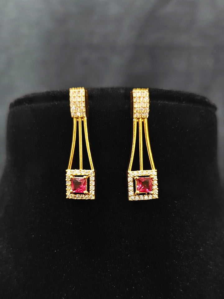 Close-up of an ornate Indo-western Red (gold Polish) Collar Layered Diamond jewellery set and earrings with American Diamond and Colored Stone. Party wear outfit completed with a lightweight American diamond necklace. Reception-ready look featuring a statement American diamond jewelry set.