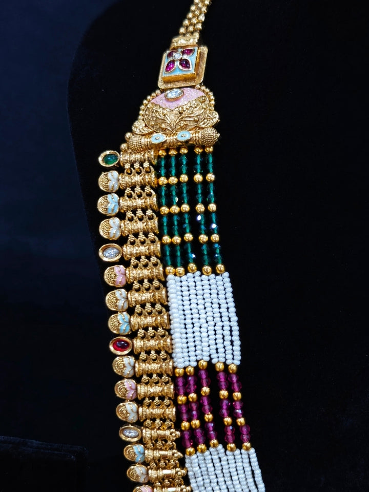 Close-up of an ornate traditional (Gold Polish) Pink & Green Long jewellery set and earrings with Pearls, Green & Pink Crystal Beads and Meenakari. Festive Diwali outfit paired with a colorful Meenakari necklace. Wedding function styling with a premium Meenakari imitation necklace.
