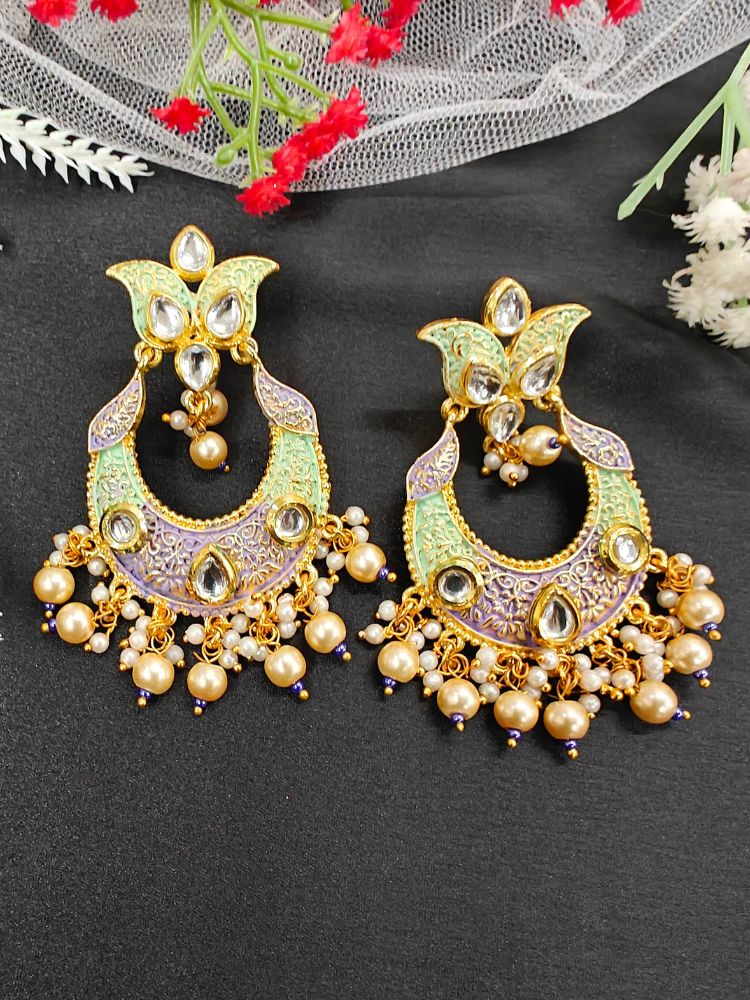 The Ekani Earrings feature ornate Kundan Meenakari work in gold and pastel sea green with Kundan and dangling pearls, beautifully displayed on black fabric with decorative flowers in the background.