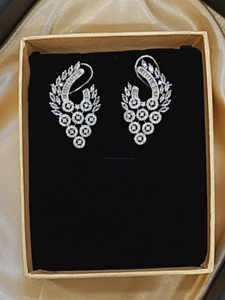 The Elaria Earrings feature ornate silver American Diamonds with intricate leaf and circular crystal designs, elegantly displayed in a black velvet-lined box—perfect white earrings to complete your wedding ceremony look.