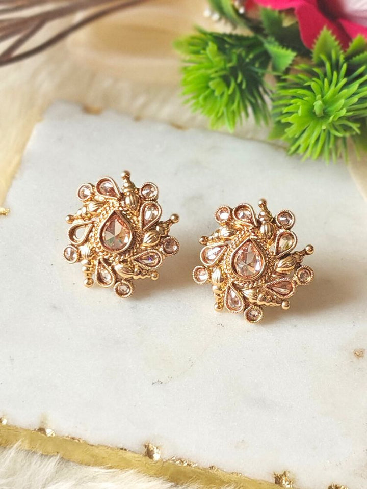 Eliza Earrings showcase intricate floral designs with reverse American diamond accents, displayed on white marble with green foliage and a red flower in the background.