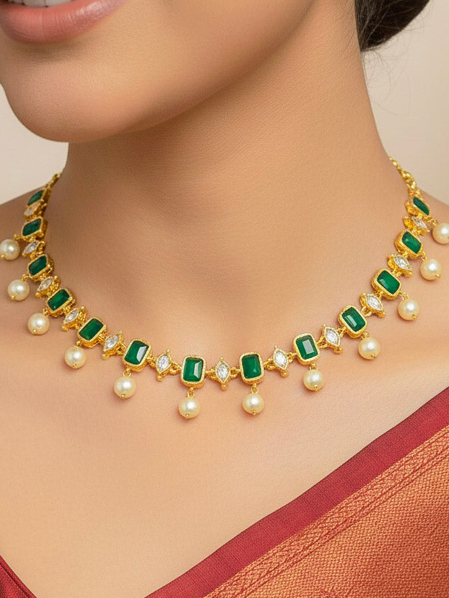 Close-up of a woman wearing an ornate traditional (Gold Polish) Emerald Green Choker jewellery set and earrings with Colored Stones, Pearl and American Diamonds. Festive Diwali outfit styled with an Colored Stones artificial necklace. Mehendi function outfit styled with a Colored Stone  necklace set.