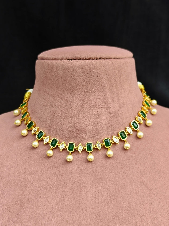 Close-up of an ornate traditional (Gold Polish) Emerald Green Choker jewellery set and earrings with Colored Stones, Pearl and American Diamonds. Festive Diwali outfit styled with an Colored Stones artificial necklace. Mehendi function outfit styled with a Colored Stone  necklace set.