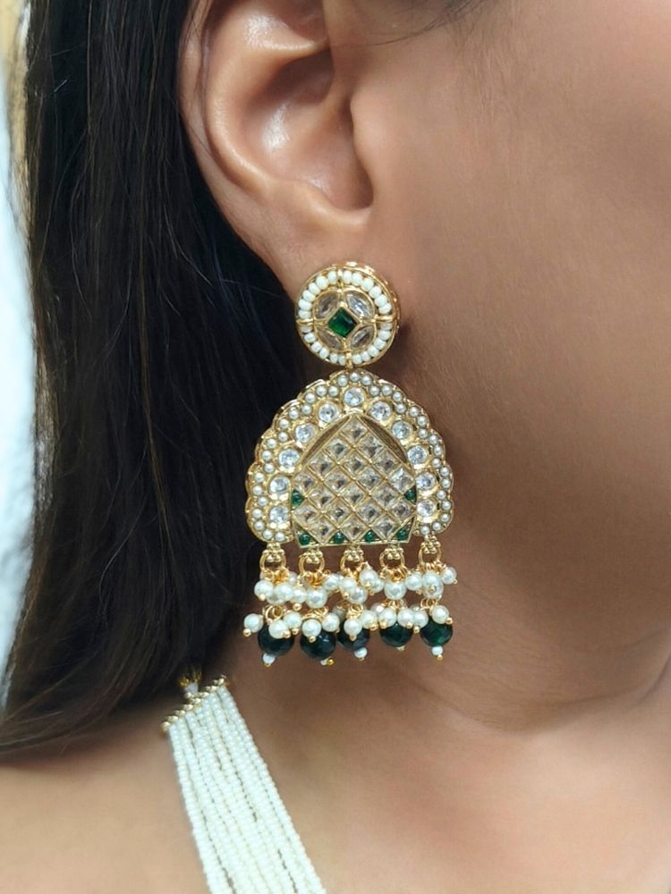 A woman wearing the Falak Necklace Set—an ornate multiple layer pearl necklace, with a large rectangular pendant made with sparkling American Diamonds and hanging pearls at the bottom, and matching gold. American diamond and pearl earrings—paired with a maroon-green saree and gold blouse, smiles slightly.