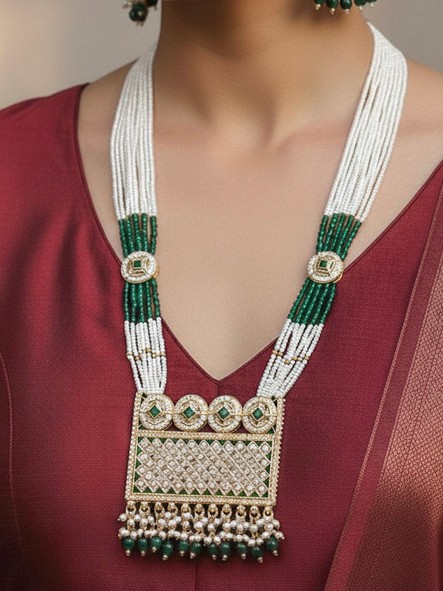Close-up of a woman wearing an ornate traditional Green Rajwadi gold Long jewellery set and earrings with American Diamonds, Pearls, Crystal stones, Green colored stones. Woman styled in a royal Rajwadi artificial necklace set for a traditional Indian wedding. Reception party look featuring a statement Rajwadi necklace.